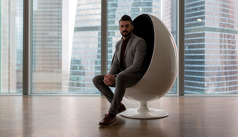 Business man wearing a grey suit sitting in modern white  Egg Chair  with buildings in the background